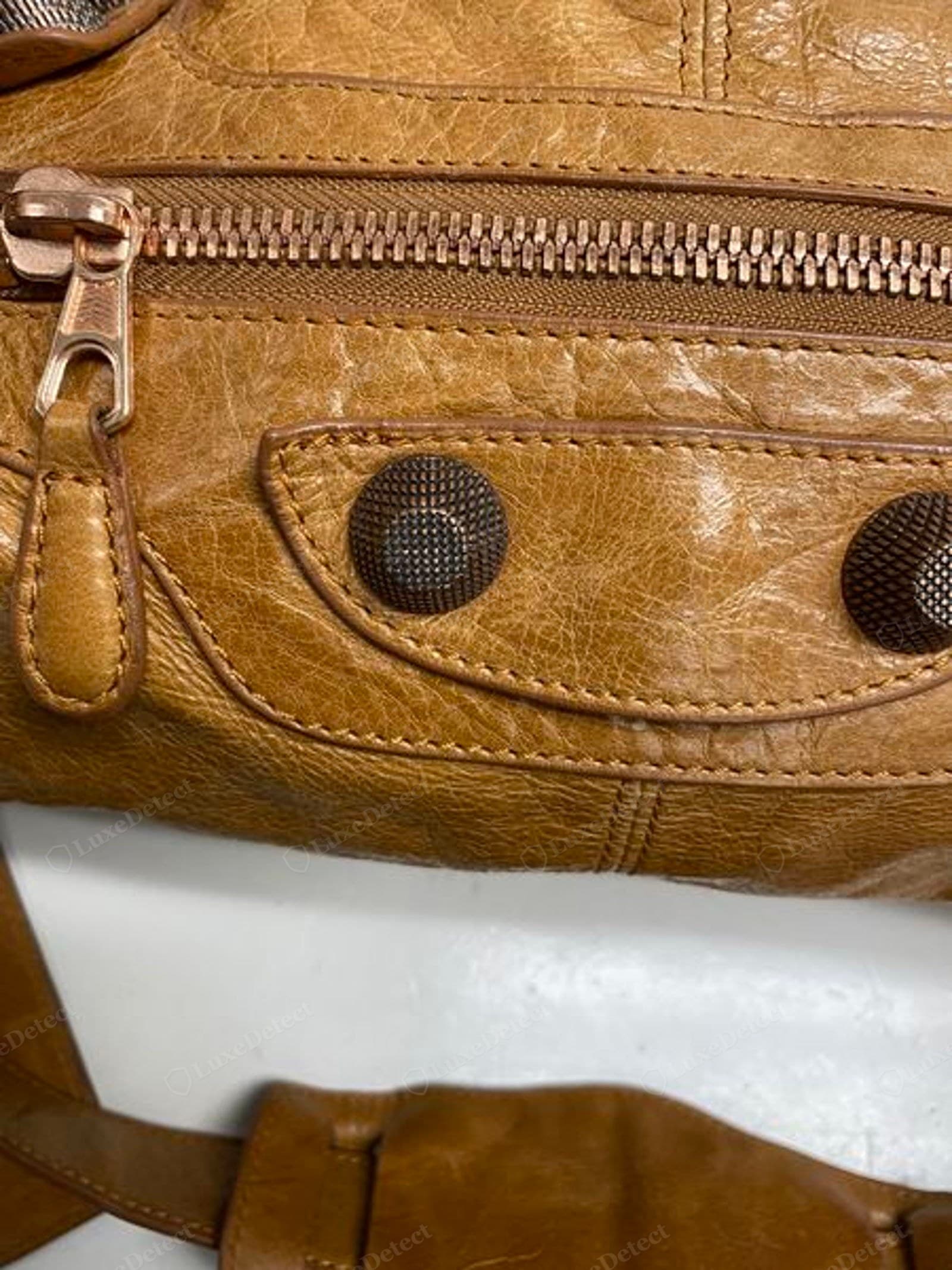 Counterfeit Balenciaga City hardware — a stud whose gold plating is corroding, red rust bleeding through, on over-glossy leather with raw fraying tab edges