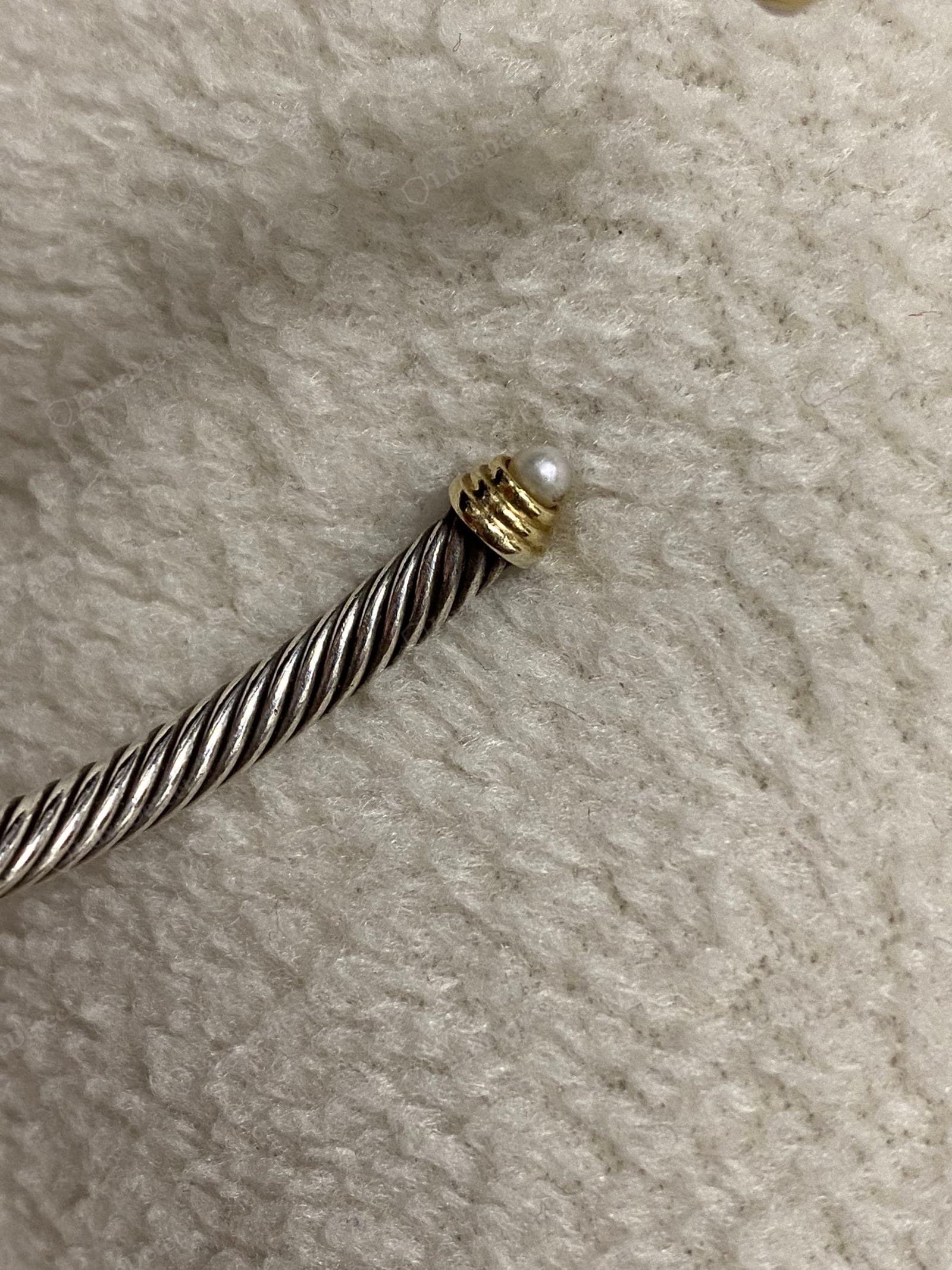 Counterfeit David Yurman end cap — a sloppily cast gold cap with a pearl set crooked and off-centre, a dark tarnished tone, and a loose stretched cable twist feeding into it
