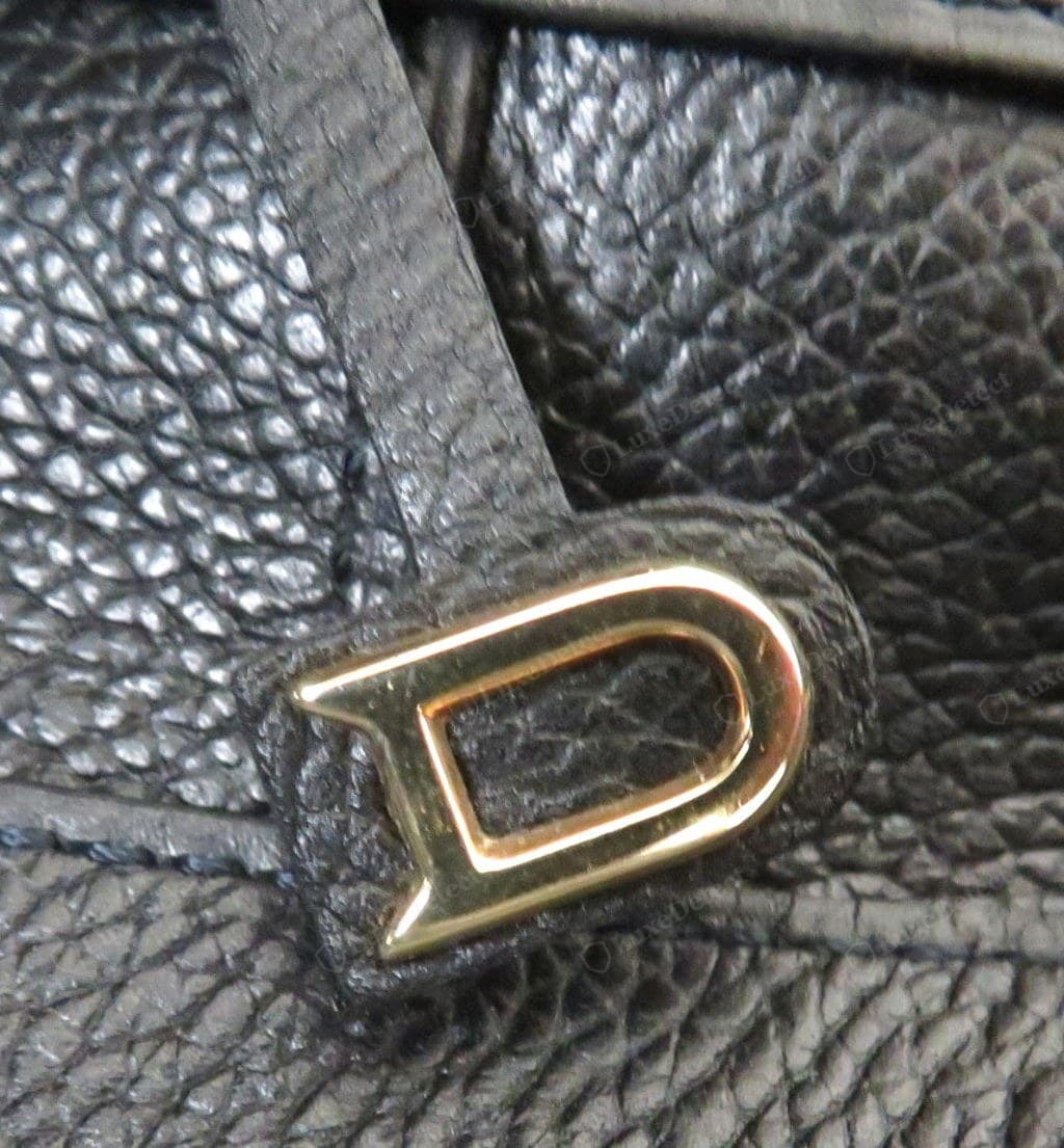 Counterfeit Delvaux clasp — lightweight with a visible seam or pitting, mushy or over-sharp edges, brassy plating, soft or absent engraving