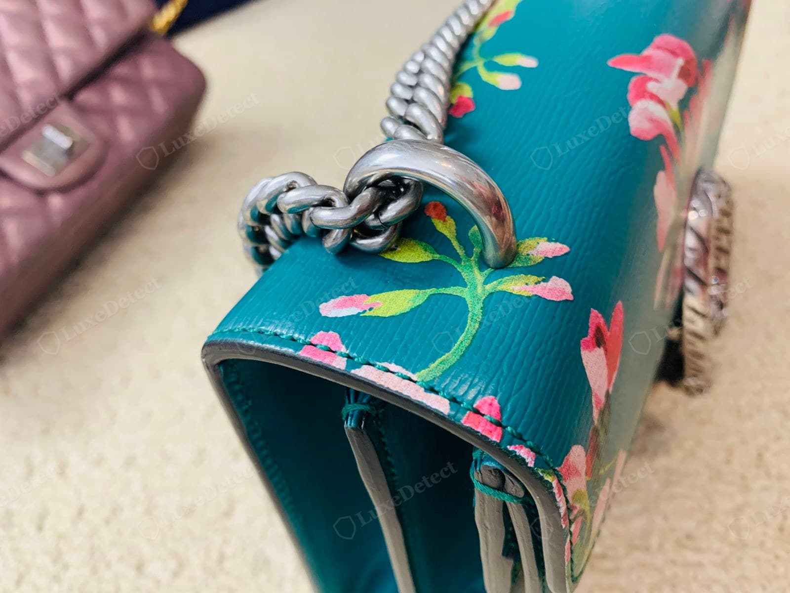 Genuine Dionysus chain: an aged-silver curb chain threading through a leather channel at the top edge of a teal Blooms flap, solid evenly finished links, tonal green stitching
