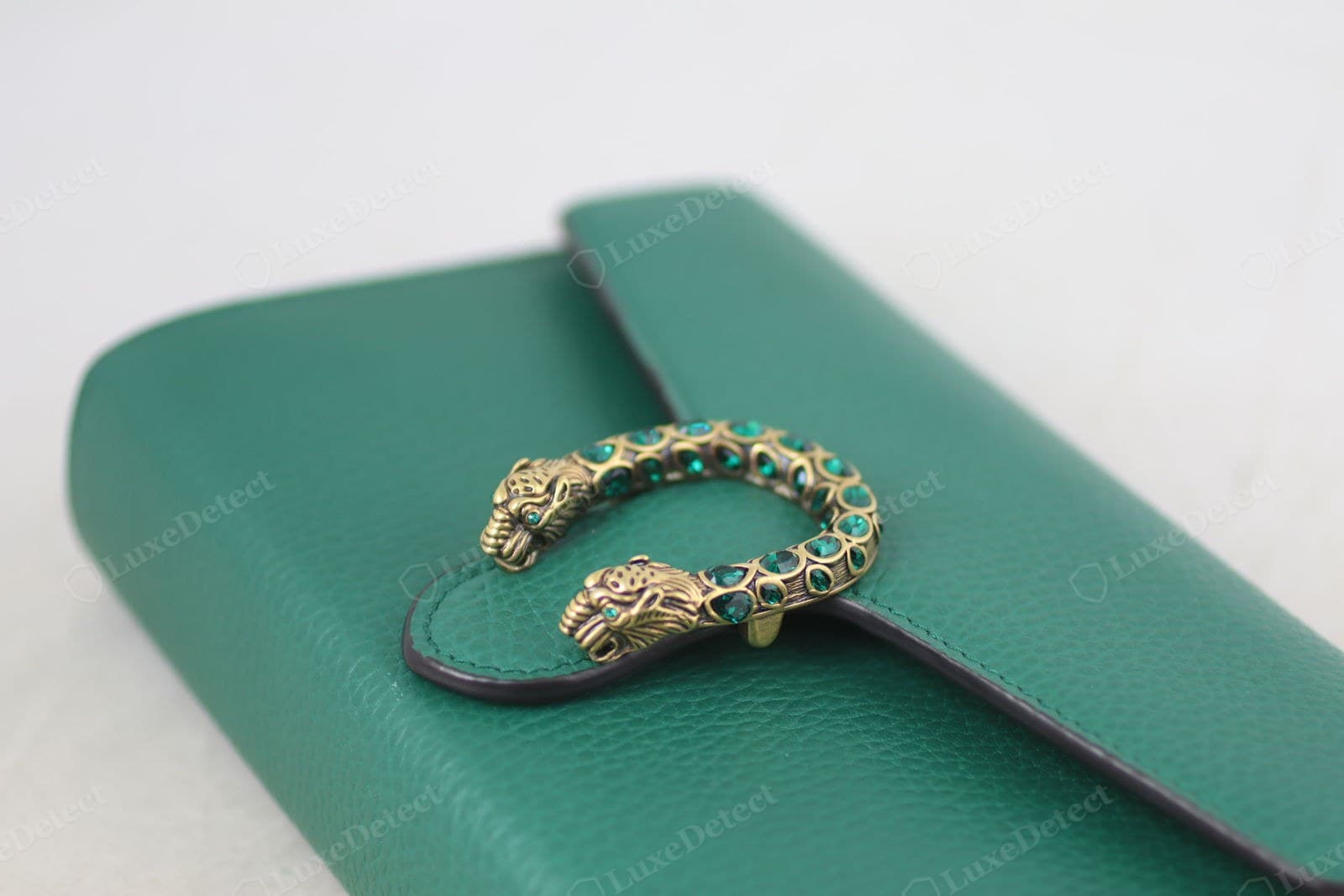Genuine Dionysus closure: the crystal-set double tiger-head spur in aged brass, green crystals individually bezel-set in a fixed pattern, deep crisp casting on the tiger heads, on fine-grain emerald leather with a burnished black edge
