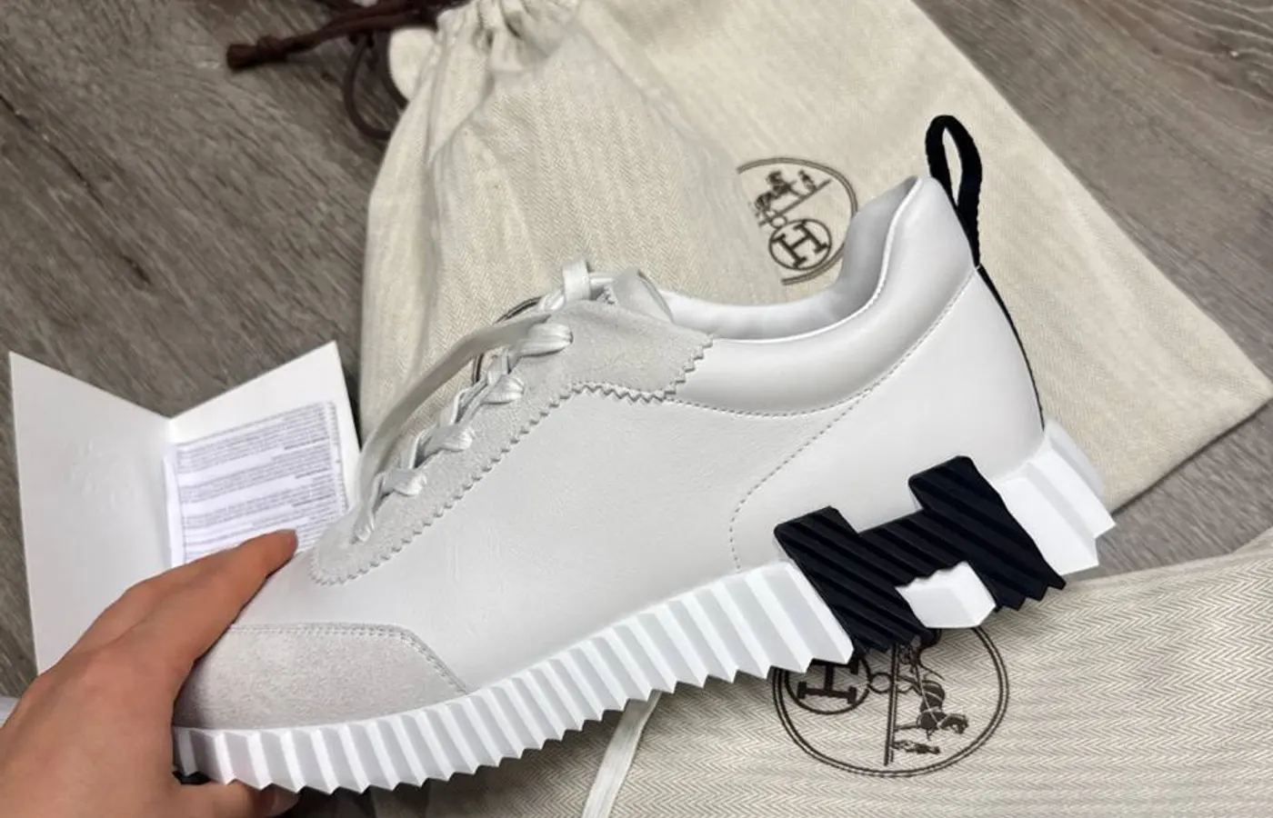 White calfskin-and-suede pair, side profile — pinked-edge suede overlays, fine even stitching, and the wave-cut sole with its sculpted H