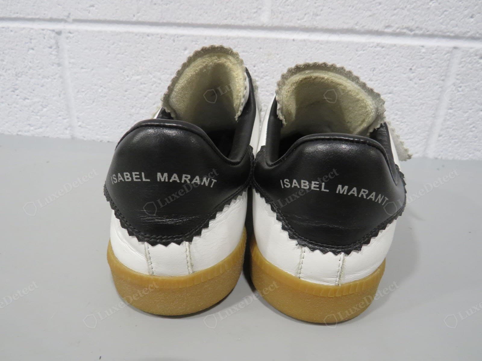 Counterfeit Isabel Marant sneakers — a heel-on view: the pinked zigzag edge where the black counter meets the white leather is uneven and crude, the heel lining already fraying, the gum sole roughly finished