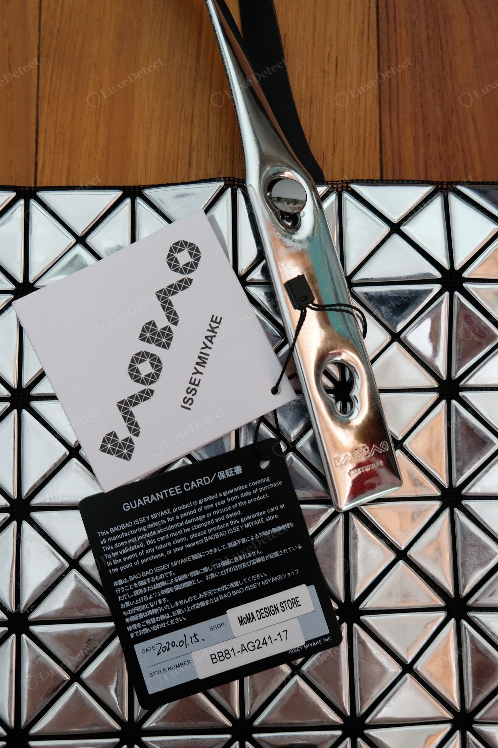 Genuine BAOBAO paperwork — the black guarantee card printed with a style number (e.g. BB81-AG241-17), a retailer stamp (here MoMA Design Store), and the geometric-logo hang tag