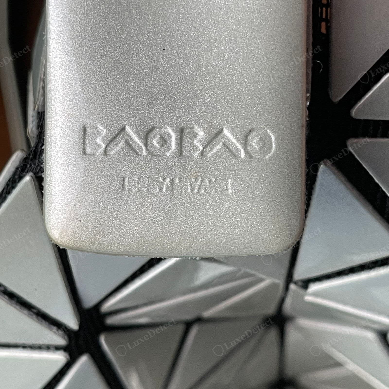 Counterfeit BAOBAO zip pull — a grainy matte casting, shallow mushy lettering with a dot inside the O's, and a barely legible, misaligned "ISSEY MIYAKE" line