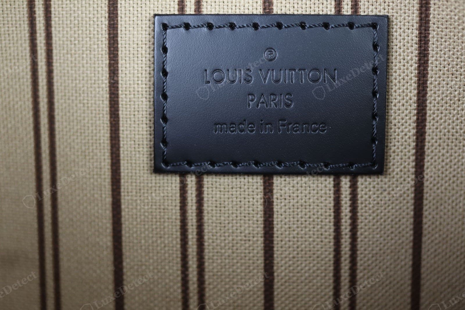 Genuine LV heat stamp (Neverfull pouch shown, same convention as the Pochette) — ® over "LOUIS VUITTON" over "PARIS" over "made in France" on a leather patch, round Os, near-touching T tops, an even shallow press, hand-stitched border