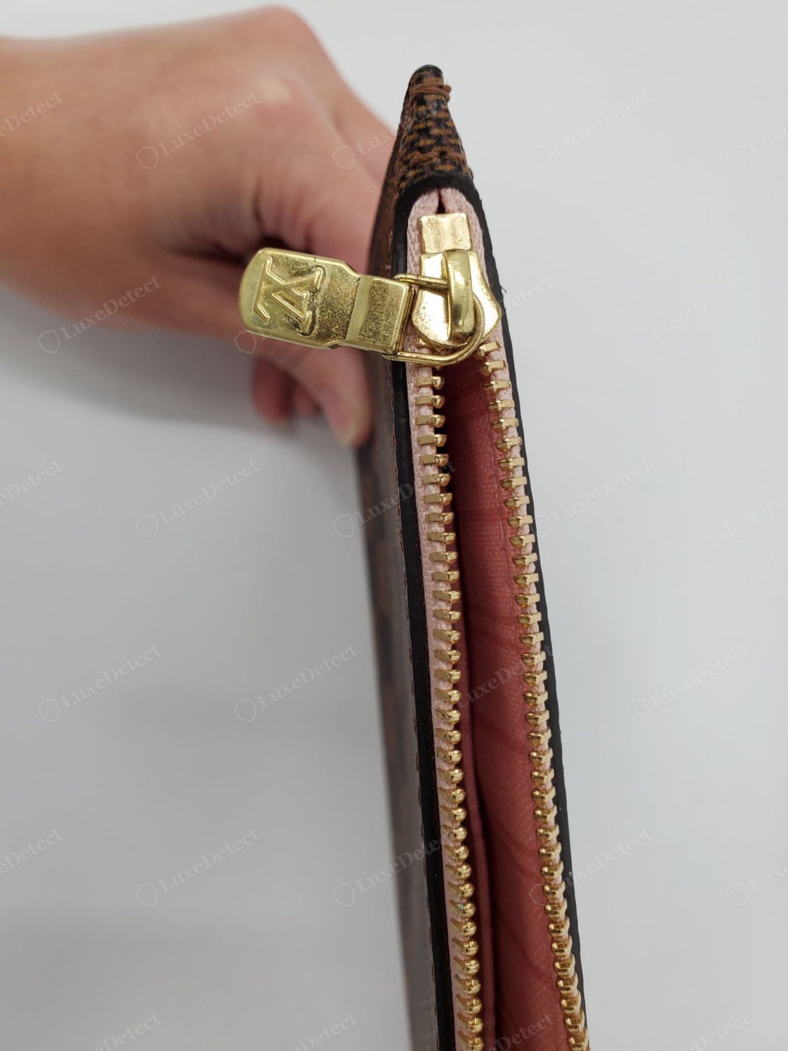Counterfeit LV zipper pull — the "LV"-embossed brass pull is worn through to raw metal, loosely and crookedly attached; a genuine pull keeps its finish with a crisp LV emboss