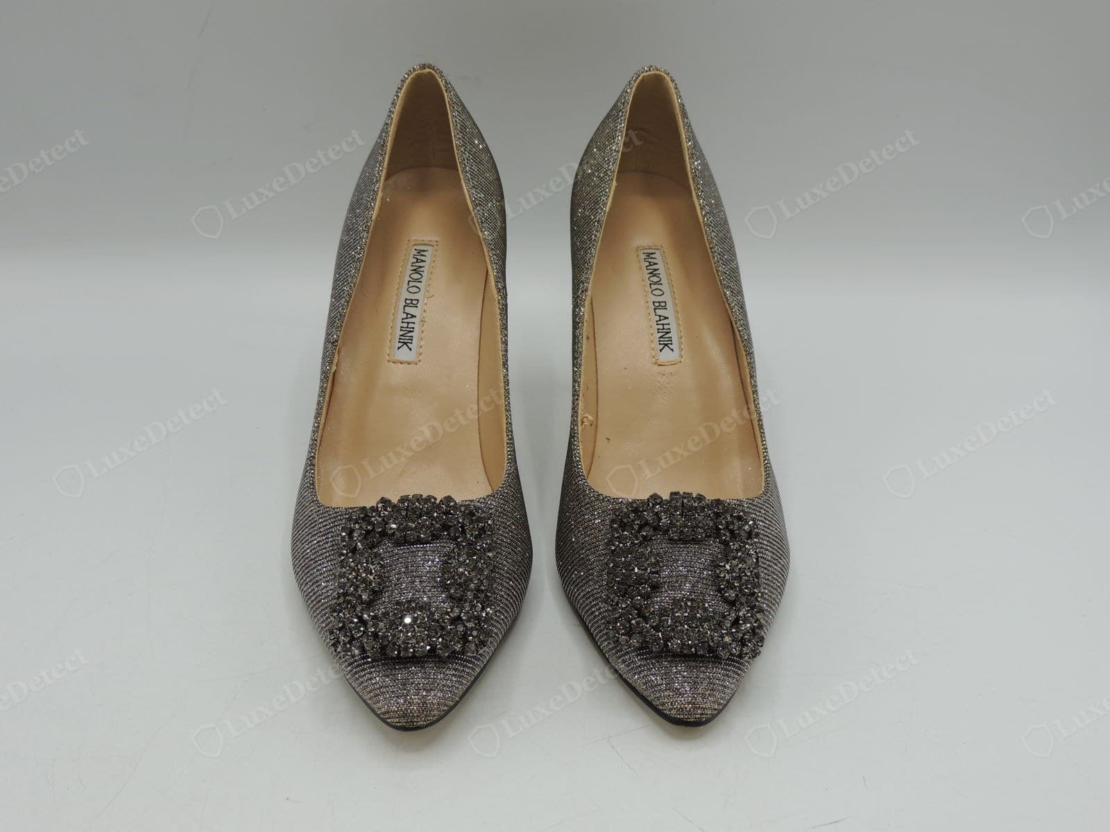 Counterfeit Manolo Blahnik Hangisi buckle — a pair of fakes with dull grey smoky "crystals" that lack the clear sparkle, and an insole label that sits crooked in its recess
