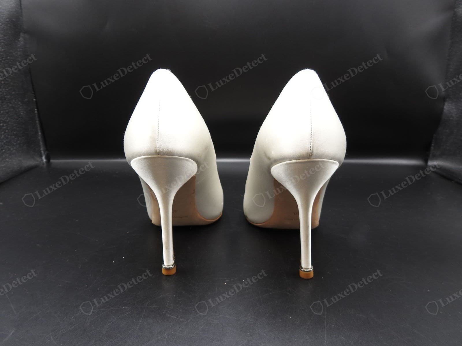 Genuine Manolo Blahnik last — a heel-on view of ivory satin pumps showing the slim precisely pitched stiletto heels, the low-cut topline, and the two shoes identical in shape