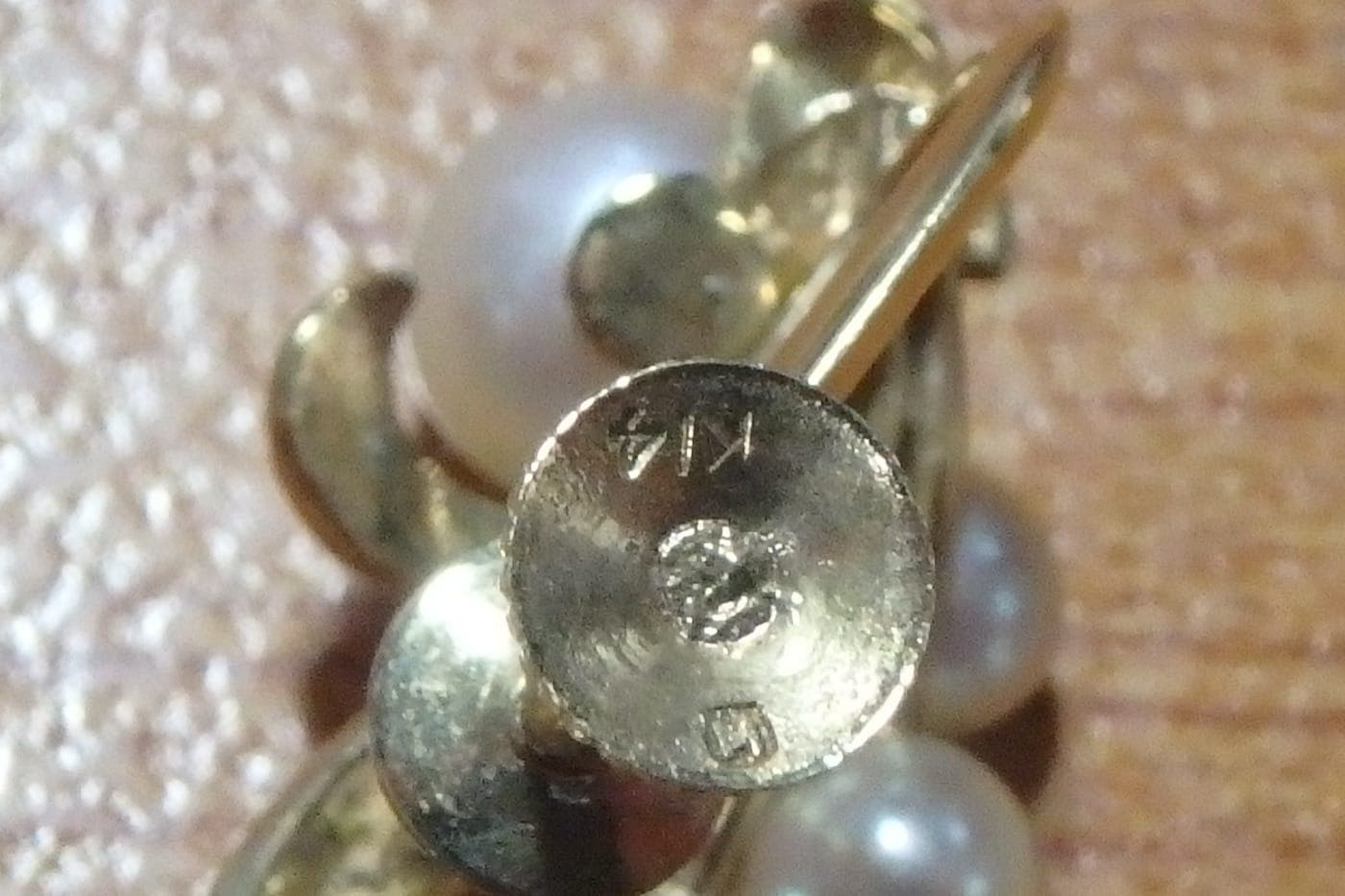 Counterfeit Mikimoto earring fitting stamped "K14". Gold does not corrode, so the green verdigris around the mark is decisive on its own — the fitting is plated base metal, and the "K14" stamp is false.