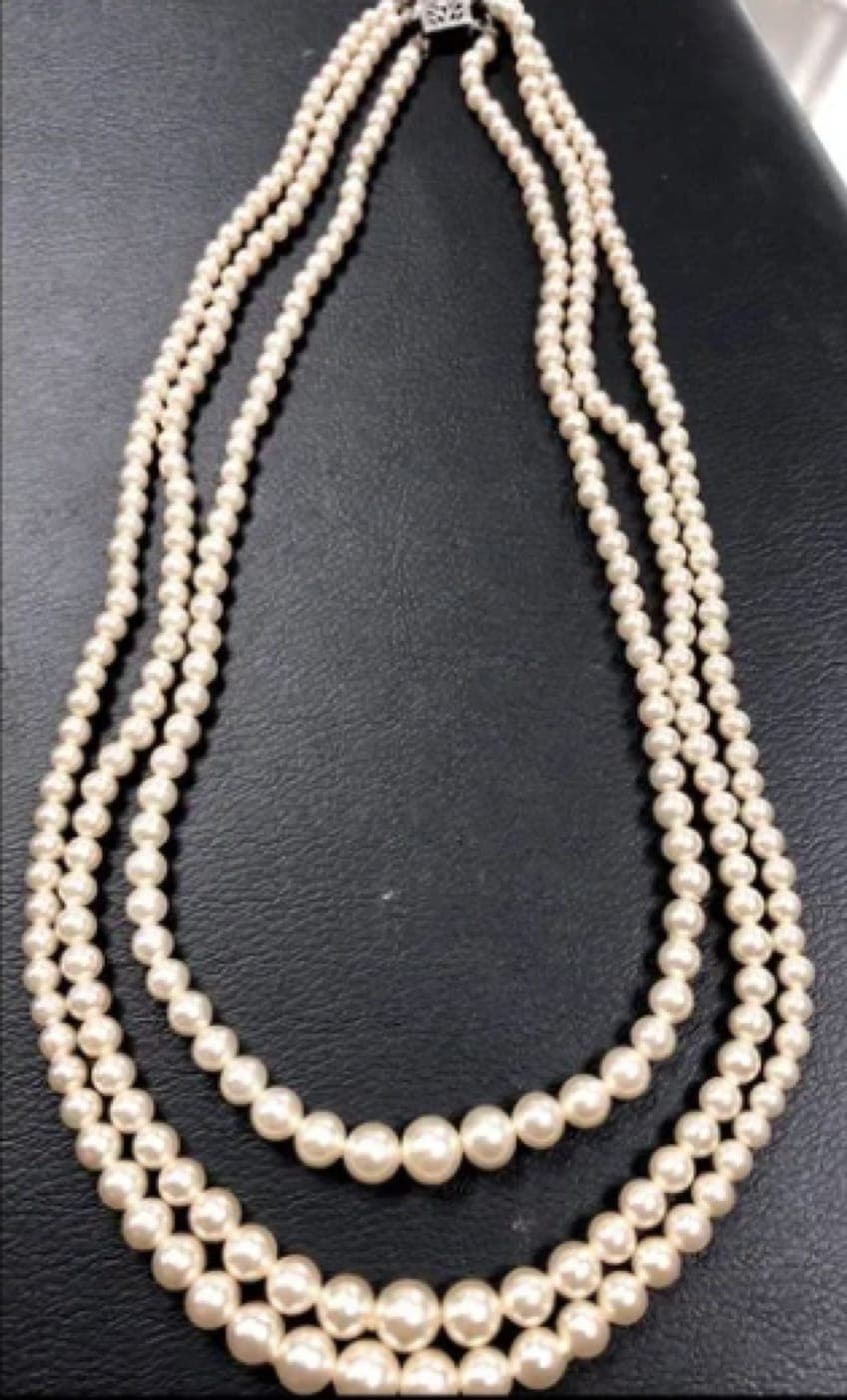 Counterfeit Mikimoto three-strand necklace. The pearls carry a soft, chalky glow with no sharp reflection, and luster and tone drift visibly from pearl to pearl — the opposite of Mikimoto's matched, mirror-bright grading standard.