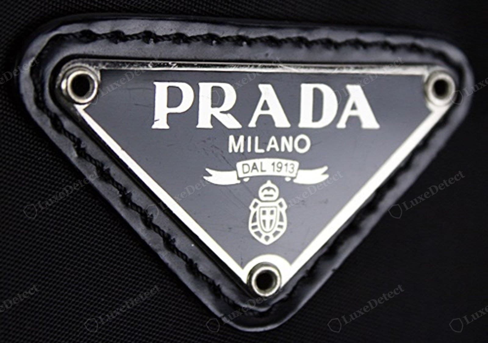 Counterfeit Prada Re-Edition triangle — domed or matte enamel, furry lettering, plaque lifting at a corner