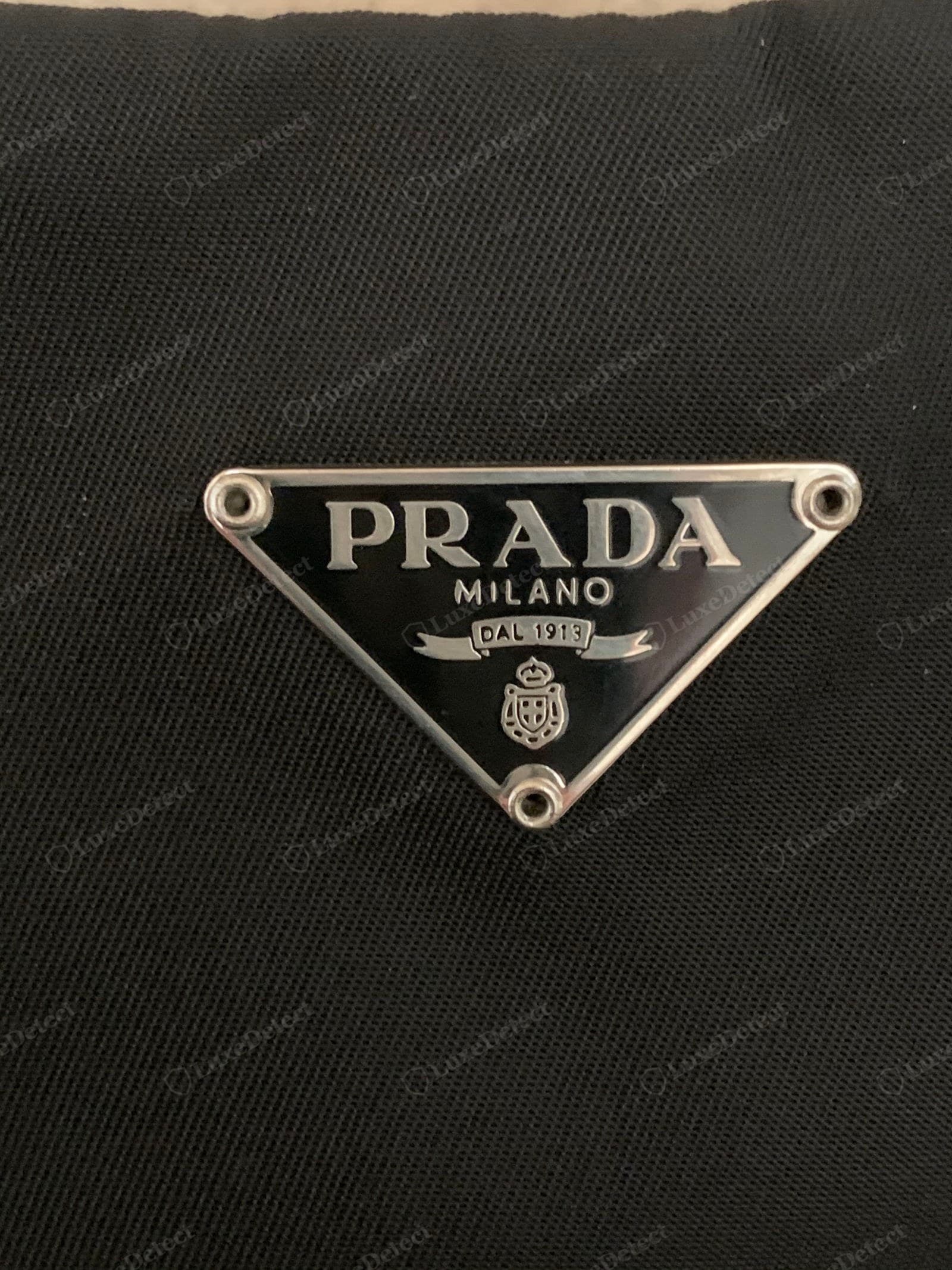 Genuine Prada Re-Edition triangle — glossy level enamel, crisp serif PRADA, plaque flush to the nylon