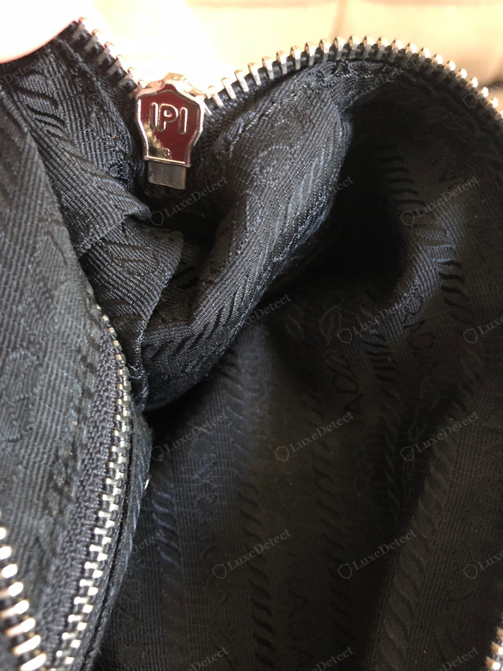 Counterfeit Prada Re-Edition zipper — no maker's mark or a crude one on the slider, a gritty action, tape in a generic black