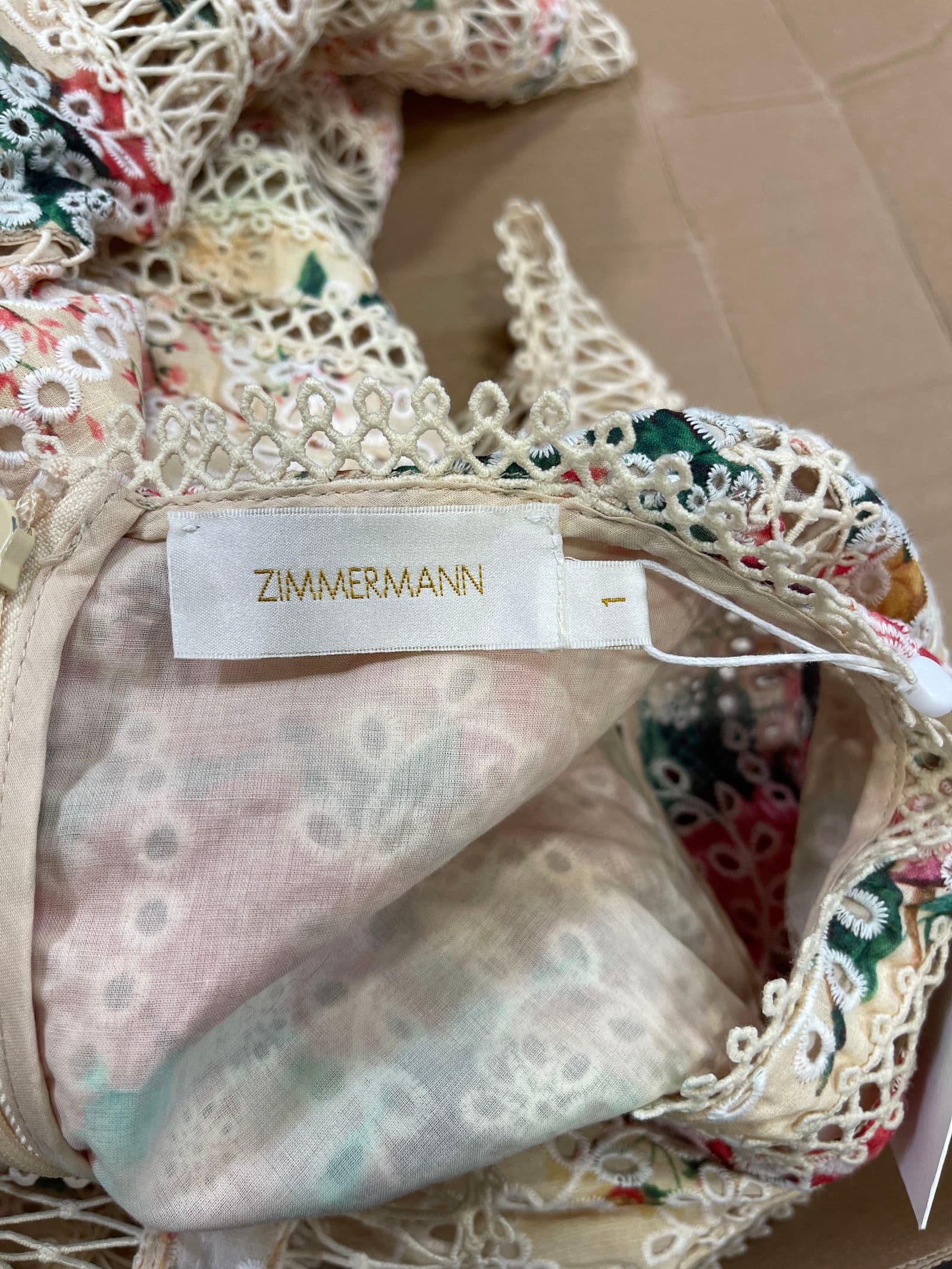 Counterfeit Zimmermann label — a closer copy on a floral dress, the gold embroidery still slightly ragged and the size tab nearly blank; pair this with the crisp genuine label above