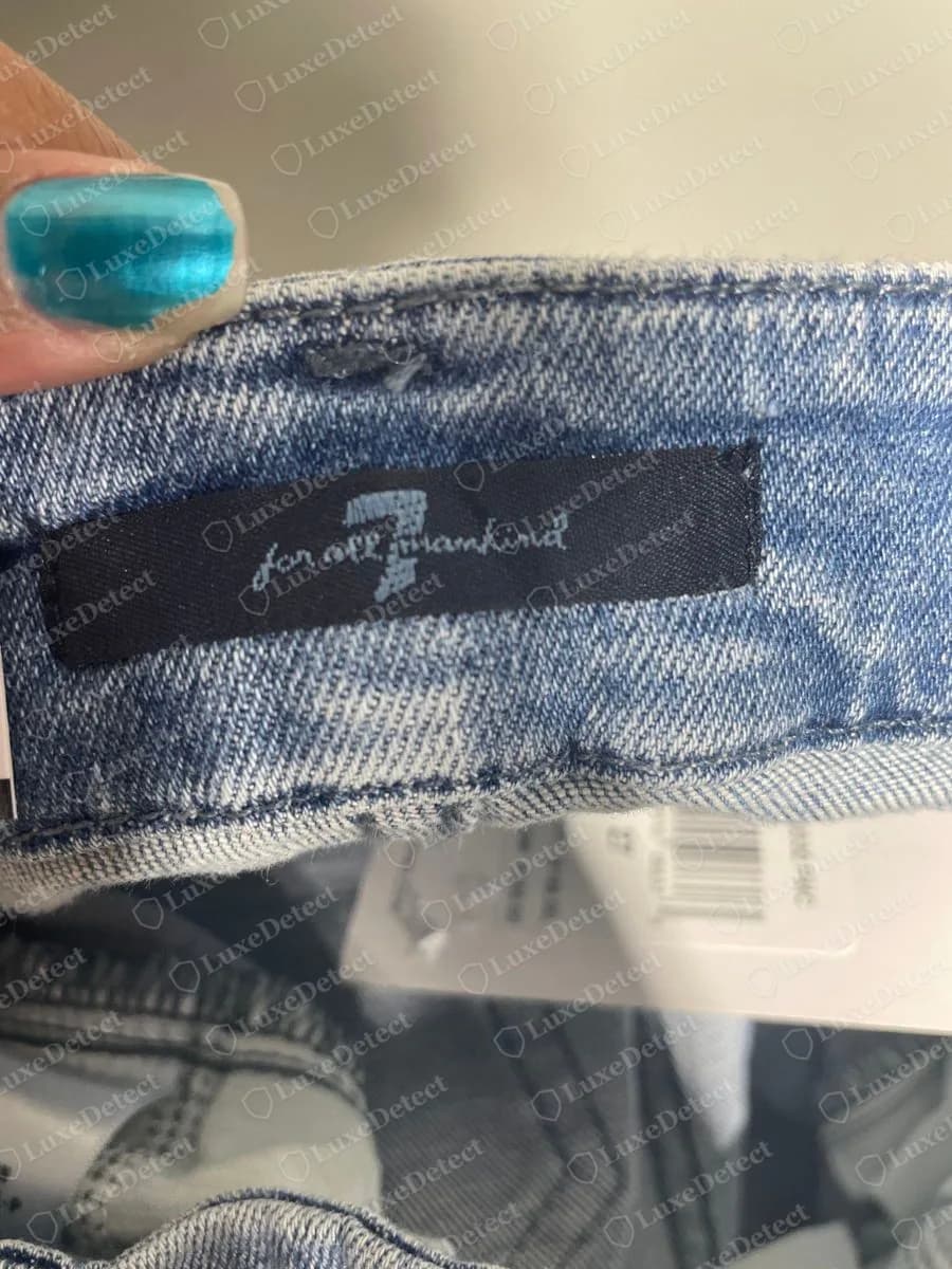 Genuine 7 For All Mankind black woven waistband label on light blue jeans, with a large 7 and for all mankind in light grey script, and a retail tag hanging below