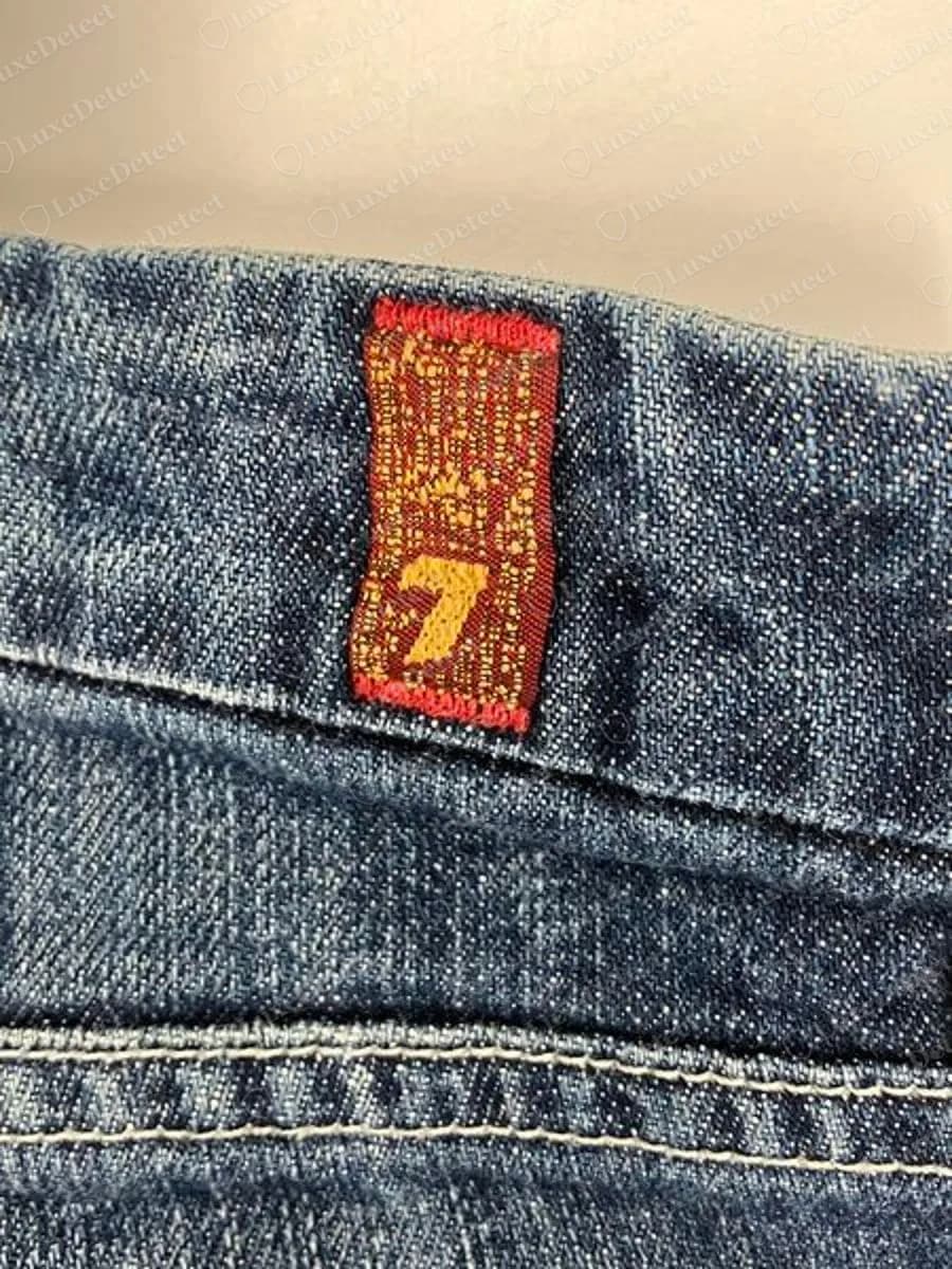 Genuine 7 For All Mankind red woven tab with a yellow 7 sewn into the back of the waistband of a pair of blue jeans