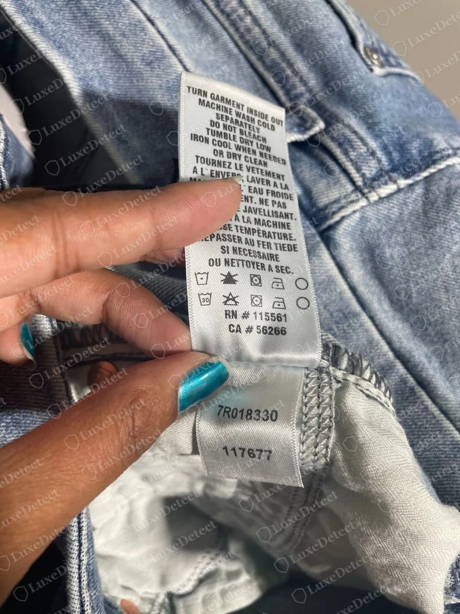 Genuine 7 For All Mankind white satin care label with English and French wash instructions, wash symbols, RN # 115561 and CA # 56266, and a second tag below printing 7R018330 and 117677