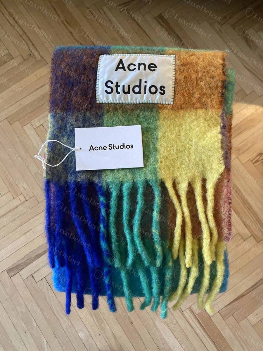 Authentique : écharpe à carreaux Acne Studios posée à plat, montrant le patch d'angle et les glands de la frange adoucis par la laine brossée