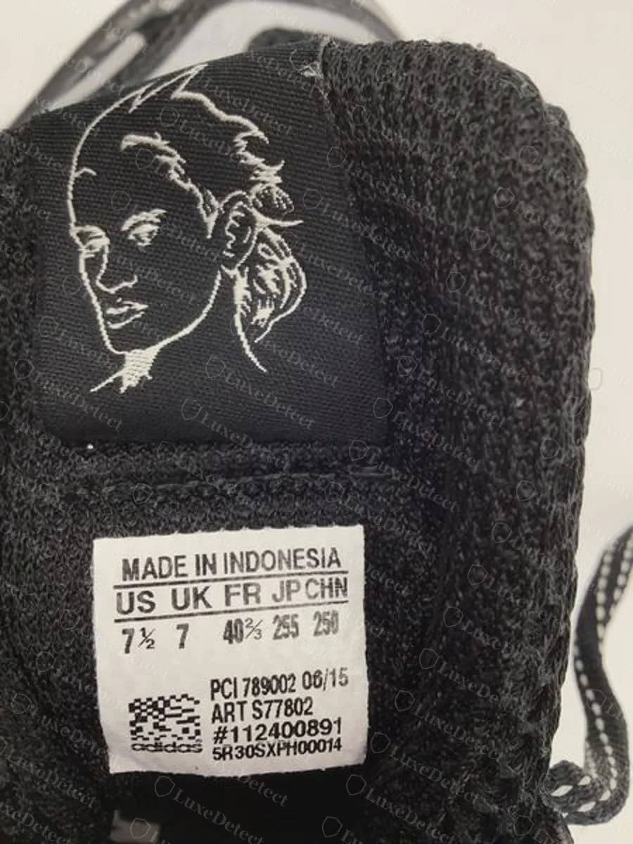 Lengüeta de una zapatilla adidas Jeremy Scott Wings 2.0 original de malla negra, con una etiqueta tejida negra que muestra un retrato blanco dibujado a línea sobre una etiqueta de talla blanca de made in Indonesia con fecha 06/15