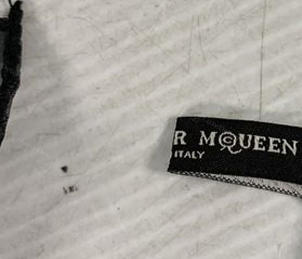 Counterfeit skull scarf hem — a flat, machine-overlocked edge with visible zigzag stitching at the tag, no rolled cord texture