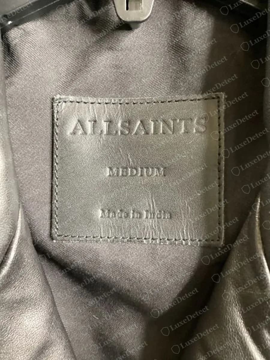 Genuine AllSaints leather neck patch embossed ALLSAINTS above the size MEDIUM and Made in India, stitched inside a black leather biker jacket