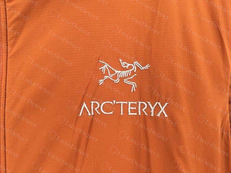 Uccello e logotipo Arc'teryx originali ricamati su un softshell arancione, con contorni puliti e punte delle penne ben distinte