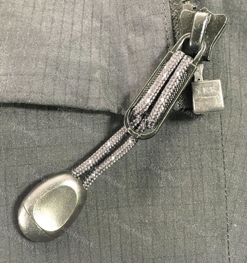 Tirador de cierre falso en el mismo cierre principal: un tirador liso en forma de gota, sin marcar, con una etiqueta YKK genérica aparte, no uno de la marca Arc'teryx.
