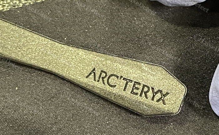 Authentic zip pull: a flat molded tab engraved "ARC'TERYX," matched to Arc'teryx's own spec.