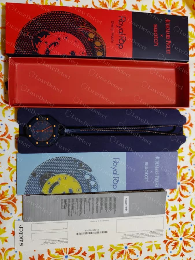 Emballage livré avec une contrefaçon : la boîte extérieure imprimée au coloris, un plateau, un fourreau de livret et un bon de garantie Swatch. Un ensemble complet comme celui-ci ne prouve rien sur la montre qu'il contient.