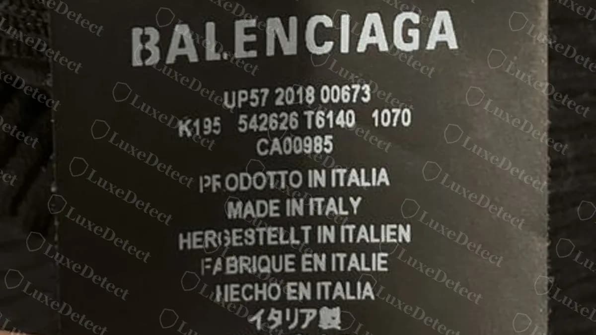 Echtes Balenciaga-Pflegeetikett auf einem schwarzen Strickteil: BALENCIAGA über einem gedruckten Style-Code, einer CA-Nummer und dem Herstellungsland Made in Italy, in mehreren Sprachen wiederholt