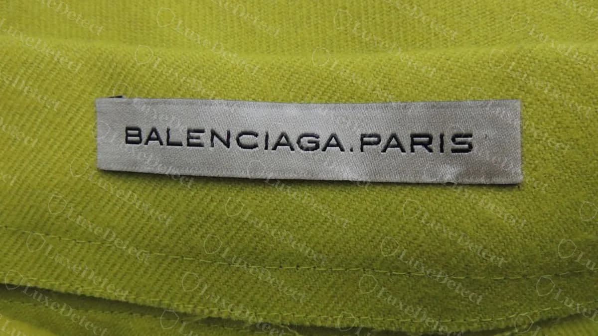 Étiquette authentique d'un ancien vêtement féminin Balenciaga sur une jupe en laine jaune-vert : ruban gris avec BALENCIAGA.PARIS en petites capitales largement espacées