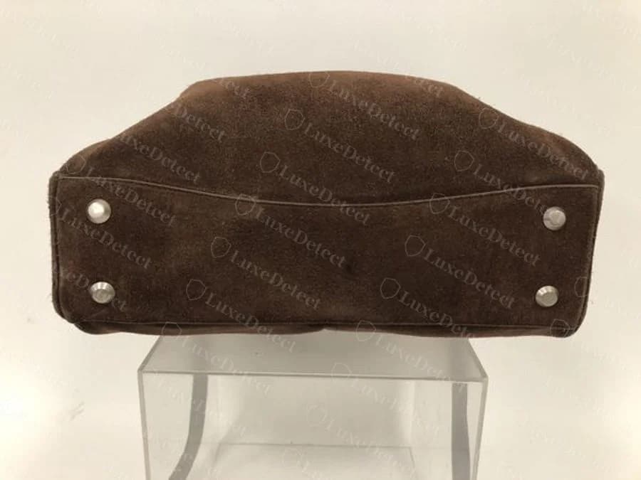 Détail de la base et des pieds d'un sac soumis comme faux : un autre coloris et du daim au lieu du cuir de veau lisse, montré pour comparer la finition et l'espacement des clous plutôt que le type de cuir