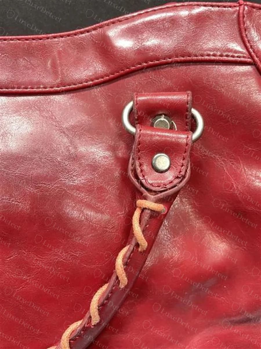Couro de uma Balenciaga City falsa — close da aba das ferragens e da tira em couro vermelho com brilho liso, lustroso e plastificado e quase nenhum amassado aleatório, a superfície continuando lisa e uniforme onde o cordeiro envelhecido original mostraria fina variação de tom