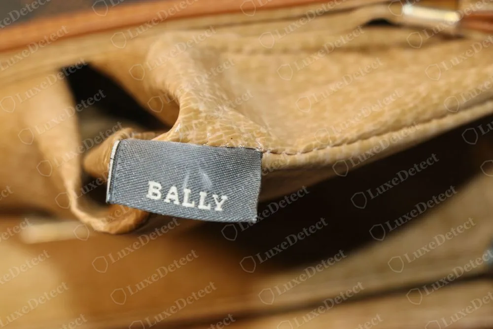 Genuine Bally grey woven interior label reading BALLY in cream capitals, sewn into the lining of a tan bag