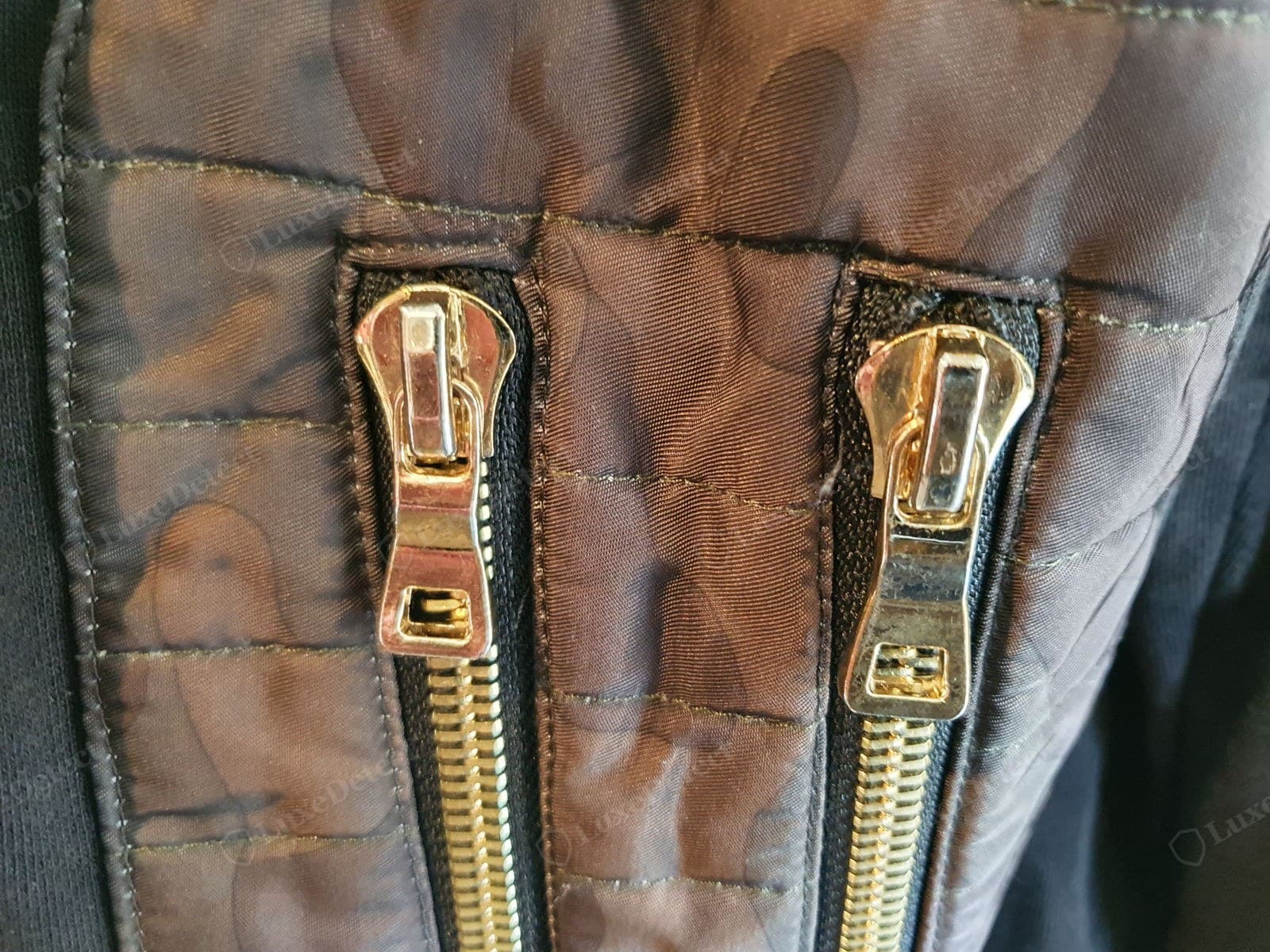 Counterfeit Balmain hardware — the two zip pulls on a fake bomber do not match: different shapes, uneven gold plating already going dull, and no maker's branding