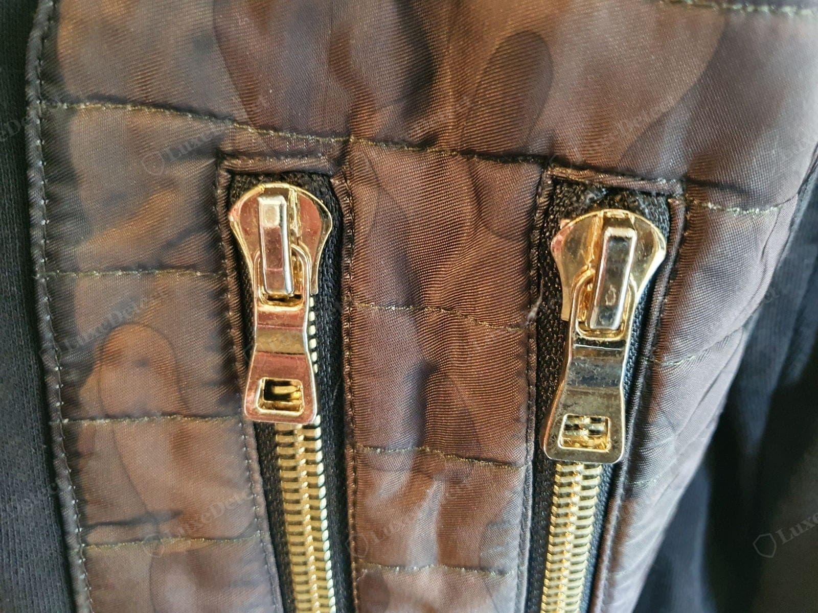 Counterfeit Balmain hardware — the two zip pulls on a fake jacket do not match: different shapes, uneven gold plating already going dull, and no maker's branding