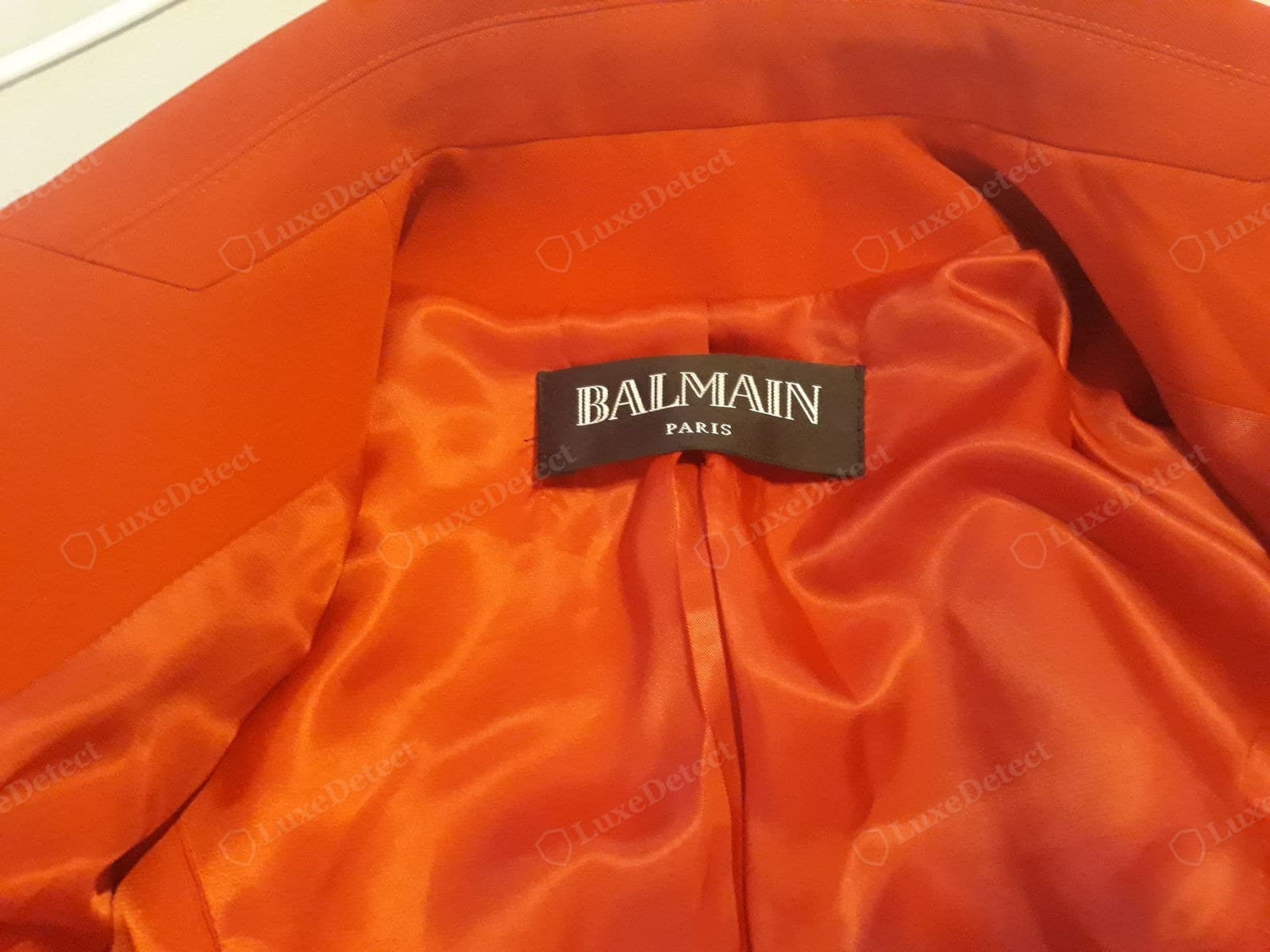 Genuine Balmain label — "BALMAIN PARIS" embroidered in the house serif capitals on a dark brown woven tab, sewn cleanly into a vivid orange satin lining