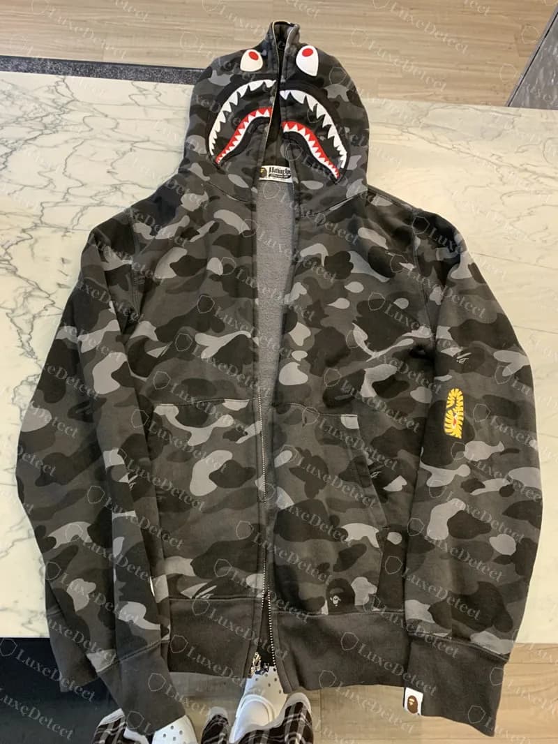 Echter BAPE Shark Full Zip Hoodie in Black Camo flach und offen ausgelegt: Camo auf dem Körper gedruckt, der Ape Head klein wiederholt, Haigesicht auf der Kapuze, gelbes Hai-Zeichen am Ärmel