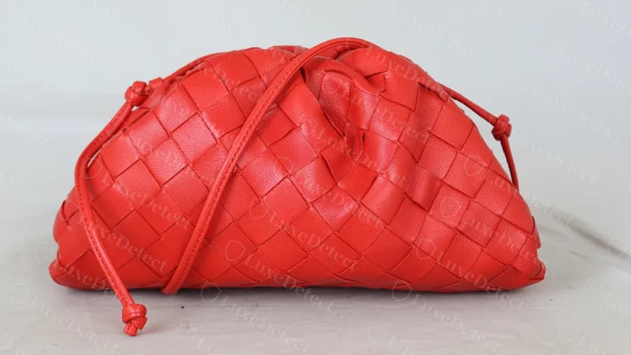 Mini Pouch intrecciato genuino en rojo: el cuerpo tejido fruncido bajo el marco, con la correa fina de cuero cruzada anudada en cada extremo