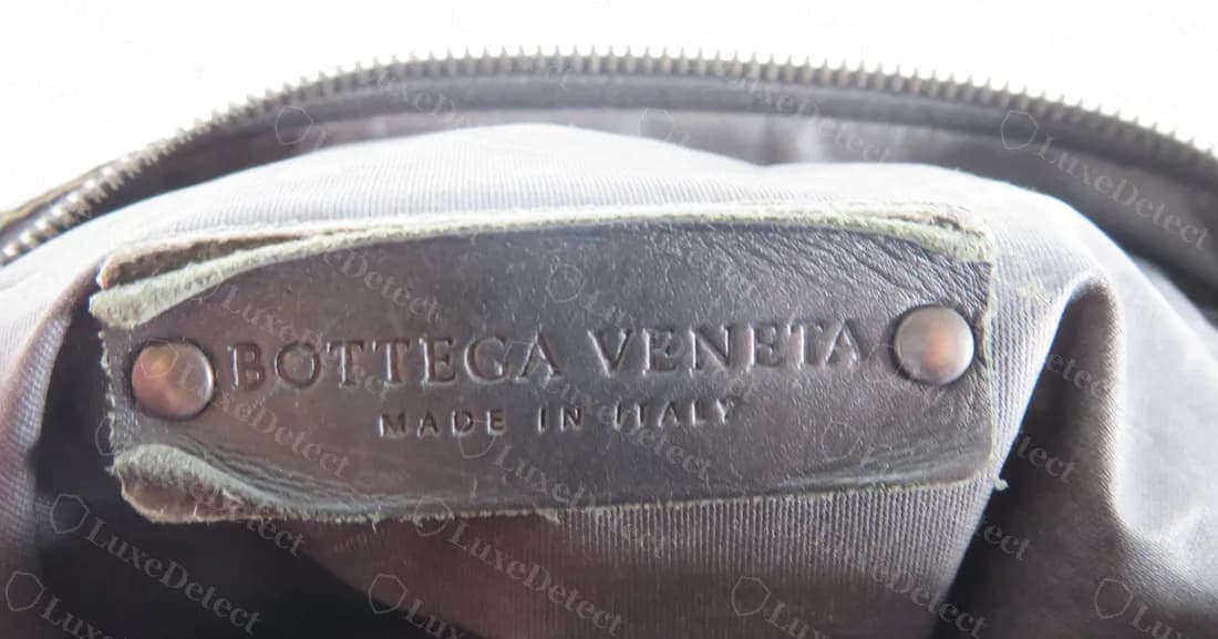 Genuine leather and metal plaque with two rivets reading BOTTEGA VENETA over MADE IN ITALY, inside a crossbody bag