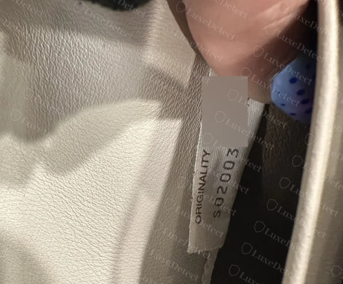 Etiqueta Originality Certified genuina que recorre en vertical una tira dentro de la ranura para tarjetas de una cartera, con el código parcialmente difuminado