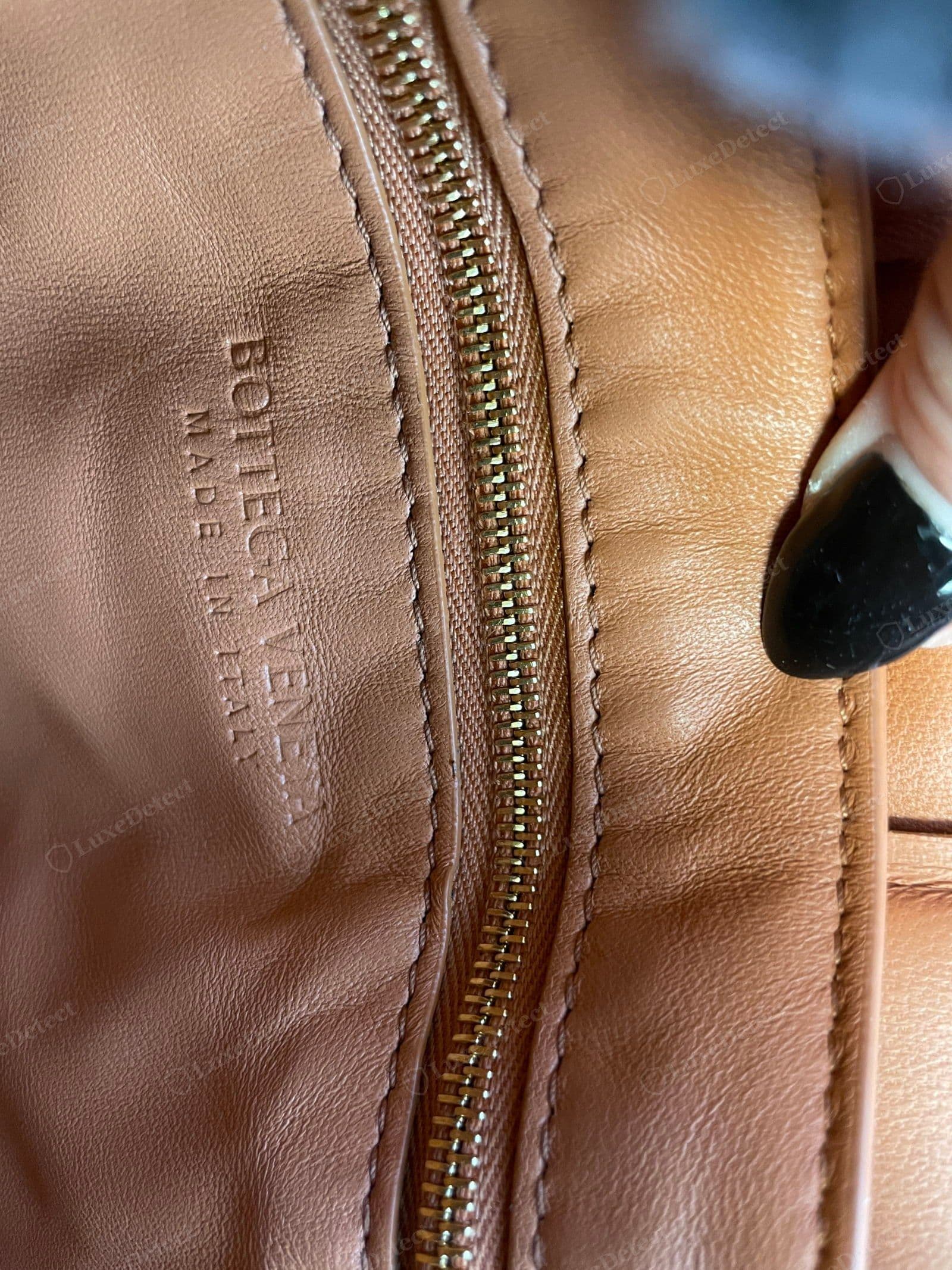 Genuine Cassette interior: "BOTTEGA VENETA / MADE IN ITALY" blind-embossed without ink into tan leather lining, beside a gold metal-tooth zip with fine even stitching