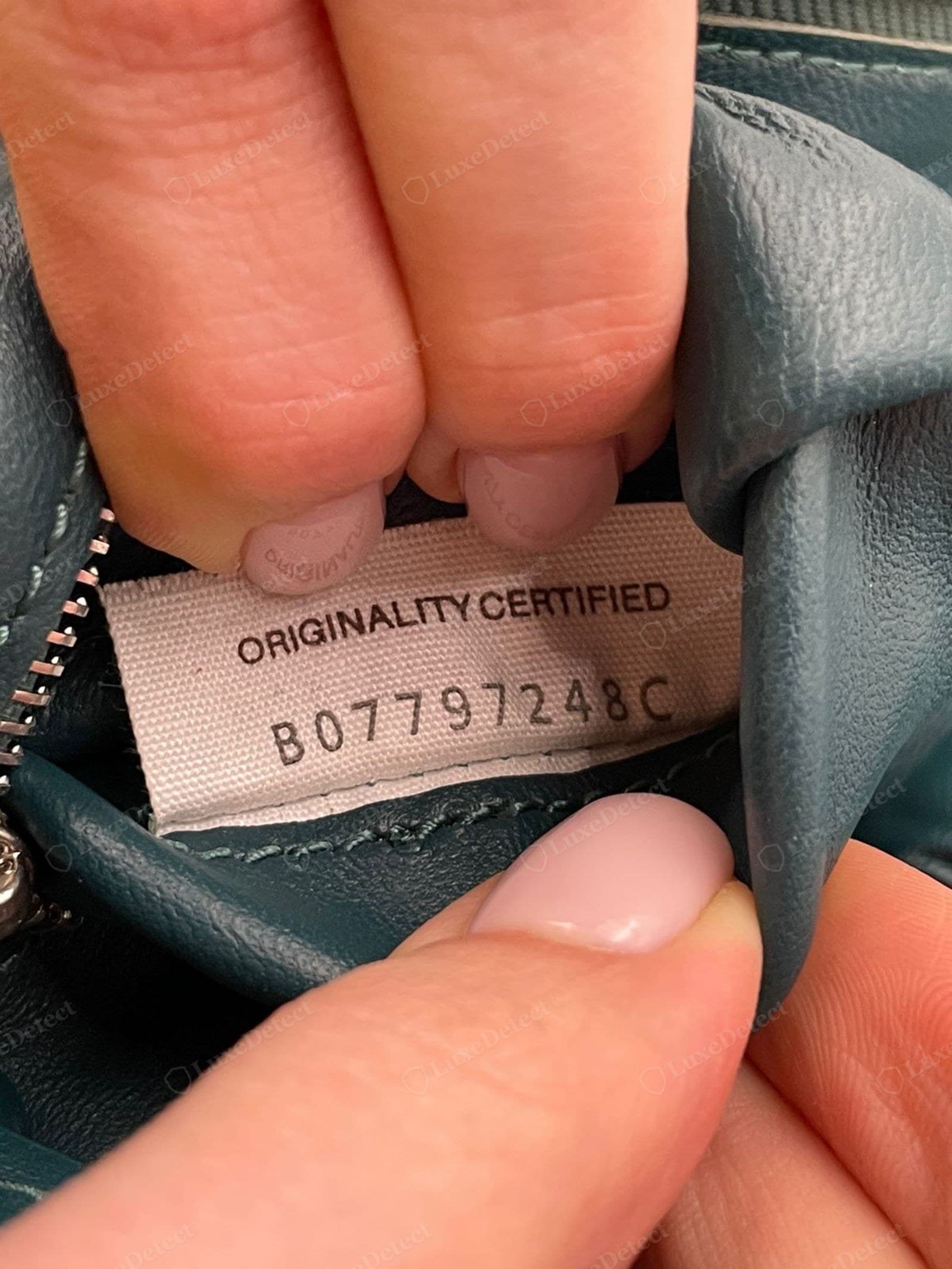 Counterfeit Cassette interior tag: a woven fabric label printed "ORIGINALITY CERTIFIED" over a long code. Bottega Veneta does not use this phrase; a self-certifying tag is a fake tell
