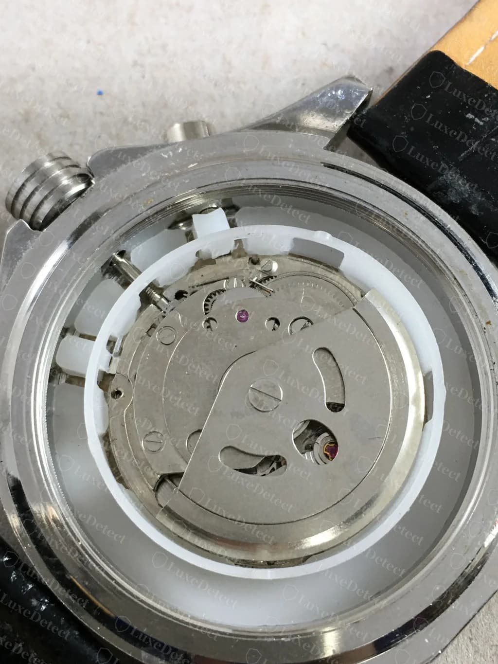 Cronógrafo falso con la firma Breitling con el fondo de caja abierto: un rotor liso sin firma y con calados, sobre un anillo espaciador de plástico blanco, sin ninguno de los acabados del rotor ni del puente firmados que muestra un Breitling original