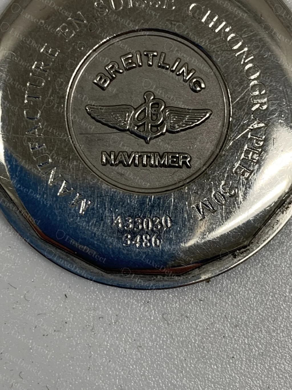 Fondo de caja de un Breitling Navitimer original: texto en relieve nítido, el logo de alas del Navitimer, la referencia (A33030) y una serie corta debajo
