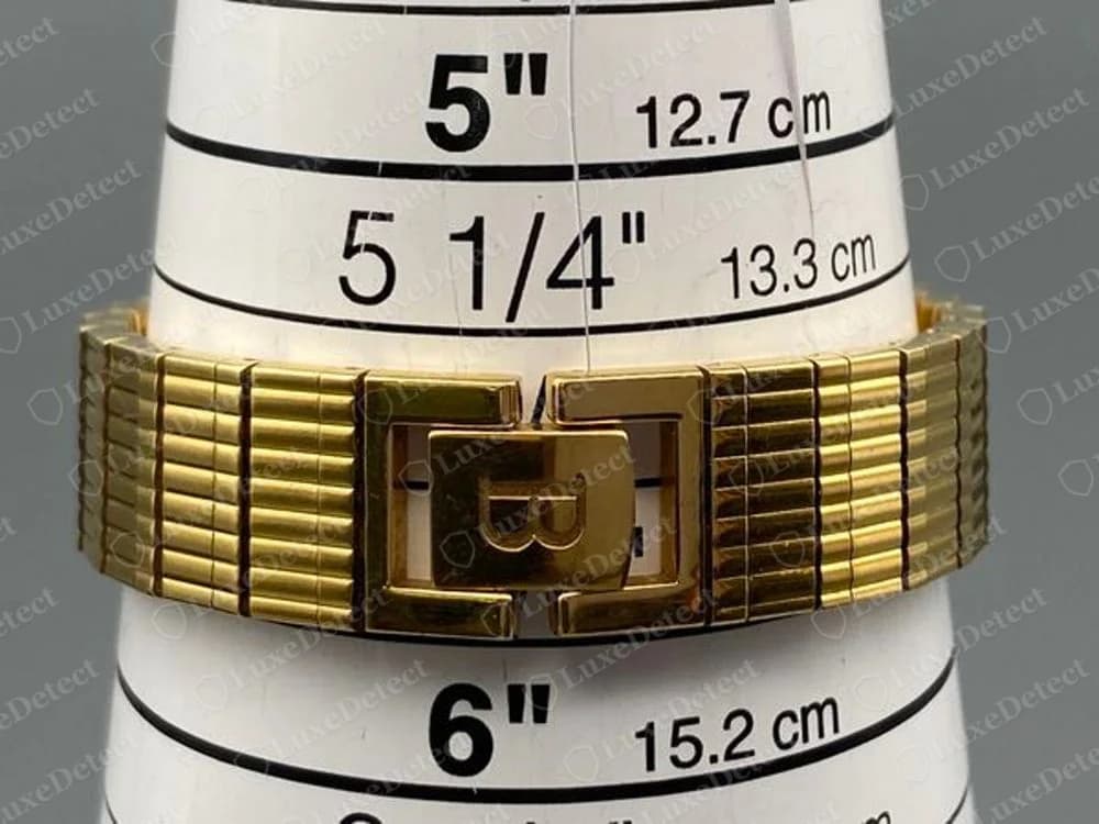 Genuine Bucherer gold-tone bracelet closed on a measuring cone, the folding clasp carrying a raised B monogram in the centre