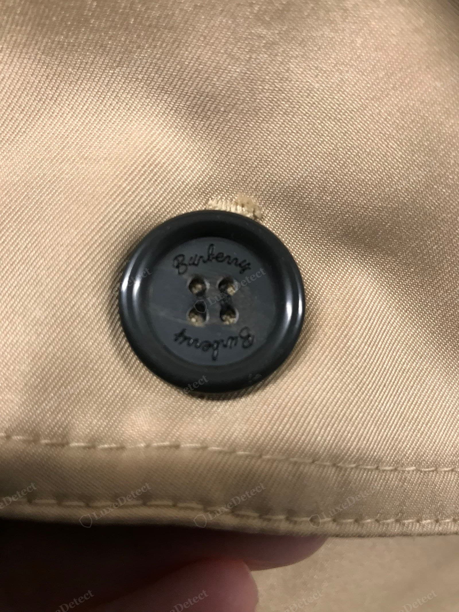 Counterfeit Burberry trench button — shallow blobby engraving, wrong typeface, plastic finish, loose