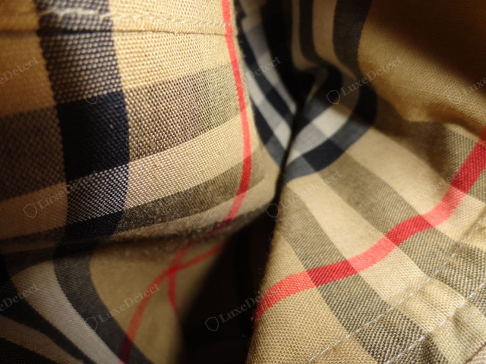 Counterfeit Burberry trench — the check lining and the stitching where a panel meets it, showing a flat printed check and wandering topstitch