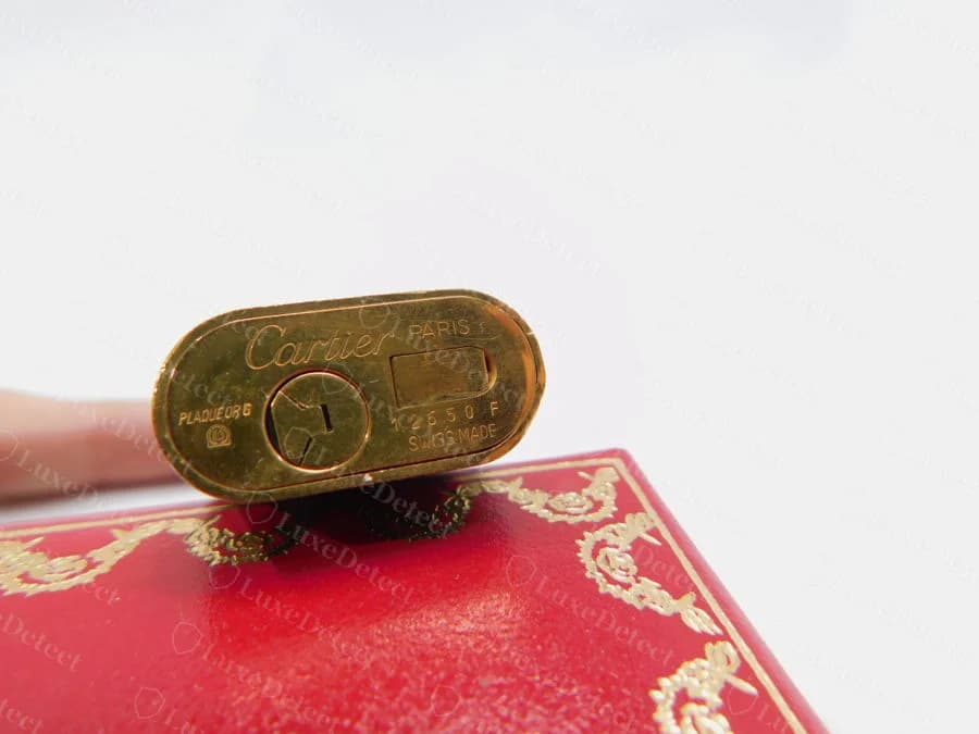 La base di un accendino Cartier originale placcato oro, con la firma Cartier, PARIS, SWISS MADE, un marchio di placcatura e un numero di serie di cinque cifre seguite da una lettera